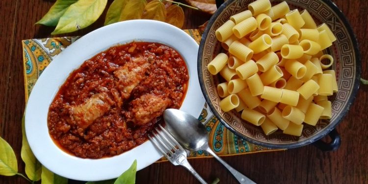 Sugo di coniglio nel piatto con pasta secca in alzatina e decorazione di foglie
